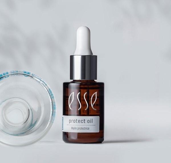 En dråpeflaske i brunt glass merket "esse protect oil" står oppreist ved siden av en klar glasskrukke som ligger på siden, mot en lys, nøytral bakgrunn.